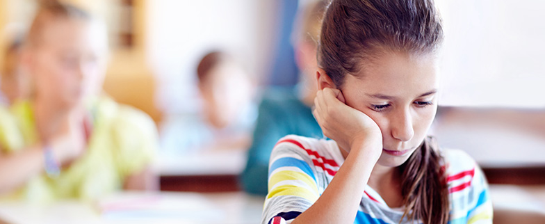 Child struggling to think at desk in classroom.